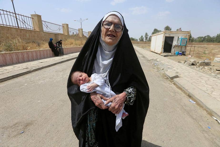 Una anciana iraquí desplazada que huyó de militantes islámicos lleva a un bebé en Mosul, Irak