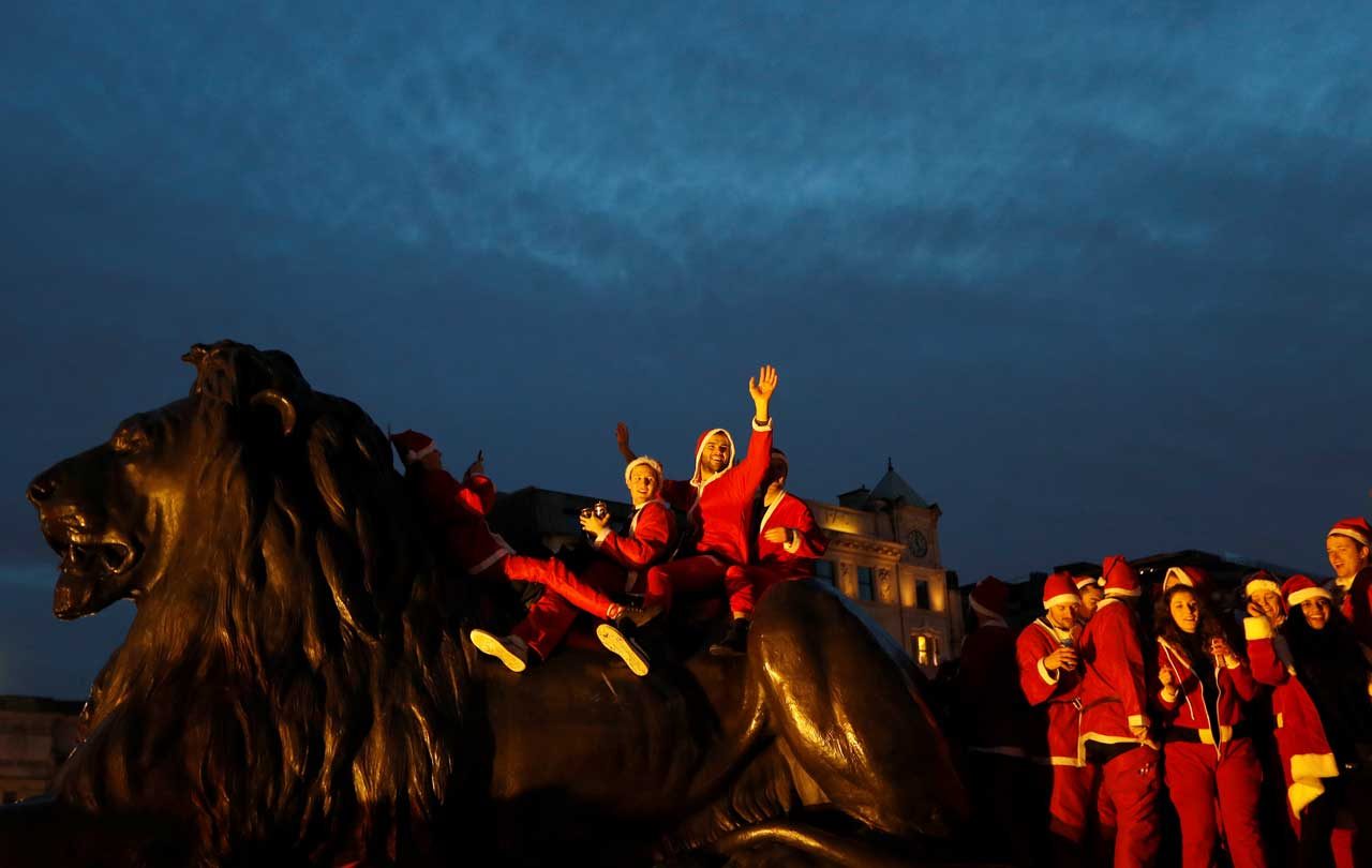Los juerguistas vestidos con trajes de Santa se sientan en un león de Trafalgar Square en Londres. REUTERS