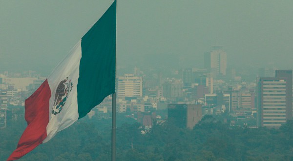 Una vista general muestra la bandera de México enfrente de unos edificios cubiertos por la contaminación atmosférica en Ciudad de México.