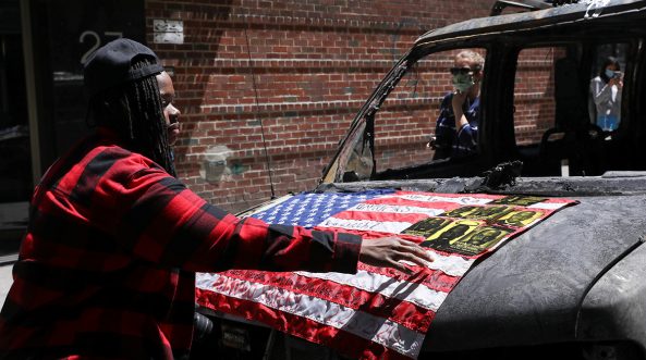 Una mujer pone una bandera en una camioneta de NYPD quemada durante los disturbios en todo el país tras la muerte en custodia policial de George Floyd. Manhattan, Nueva York, EE. UU., 31 de mayo de 2020. REUTERS / Caitlin Ochs