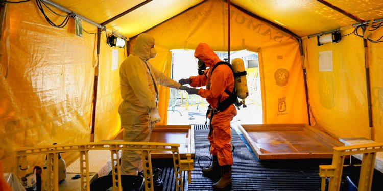 Un miembro del Servicio de Ambulancias ajusta el equipo de protección de su colega, durante la pandemia de la enfermedad del coronavirus (COVID-19), en su sede en Madrid, España. REUTERS / Juan Medina