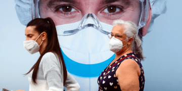 Personas, con máscaras protectoras, pasan por un anuncio de clínica dental en el barrio de Vallecas en Madrid