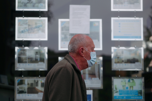 Un hombre con una máscara protectora pasa junto a una agencia inmobiliaria durante el brote de la enfermedad por coronavirus (COVID-19) en Madrid