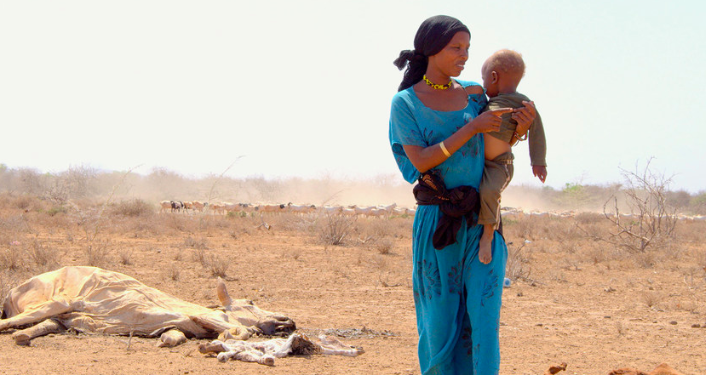 UNICEF/Oloo Una madre con su hijo en brazos caminado junto a los cadáveres del ganado muerto a causa de la grave sequía en Marsabit, en Kenya.